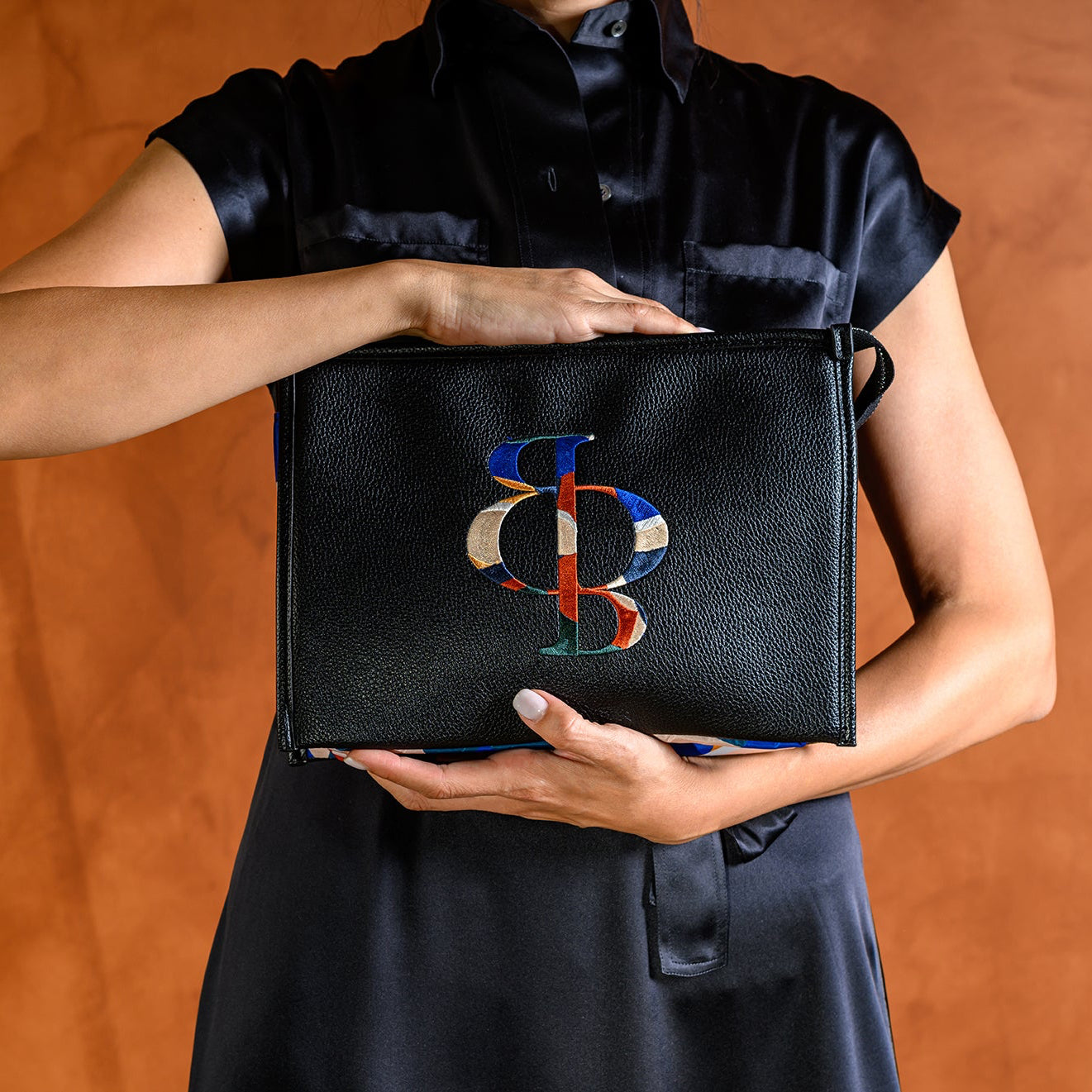 Person holding a black clutch with a colorful logo against an orange background