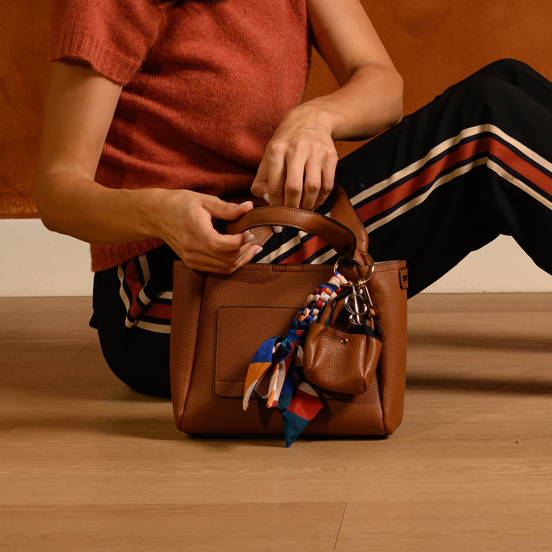 Woman sitting on the floor with a brown handbag against a brown wall.